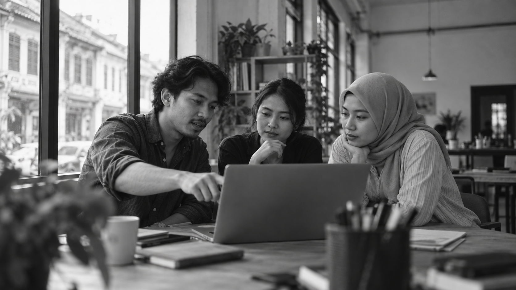 Black-and-white photo of three colleagues looking at a laptop together